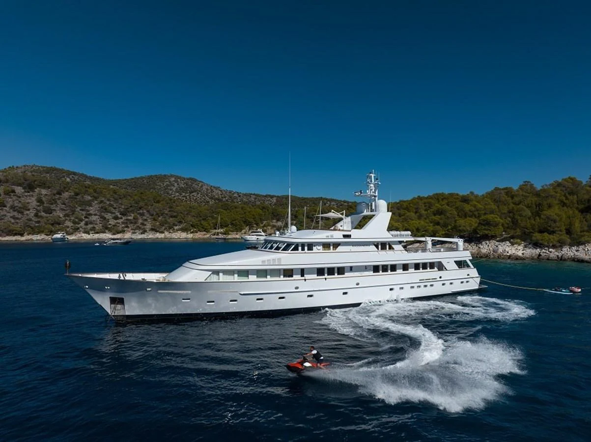 A sleek, white yacht cruises through clear blue waters, surrounded by scenic coastal hills. aboard KASSANDRA Yacht for Sale