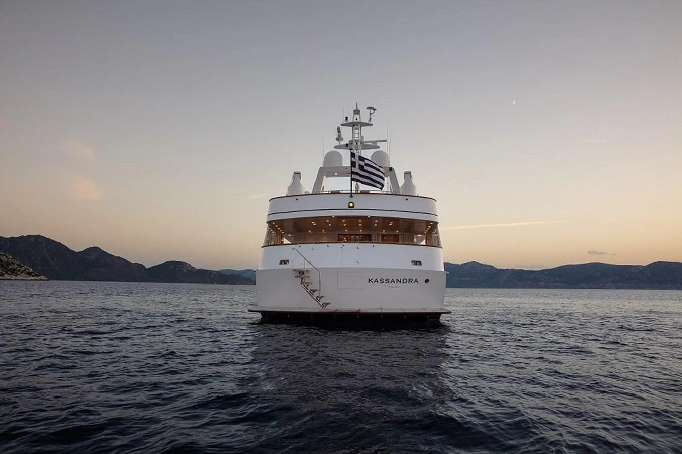 A majestic yacht is anchored on calm waters with a serene mountainous backdrop at dusk. aboard KASSANDRA Yacht for Sale