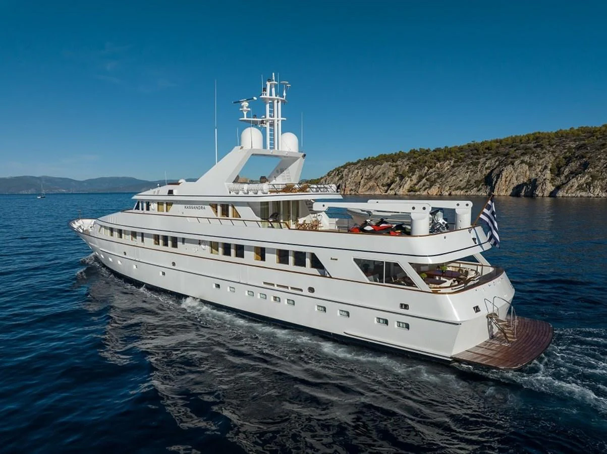 A luxurious yacht cruises through serene blue waters with a scenic coastline in the background. aboard KASSANDRA Yacht for Sale