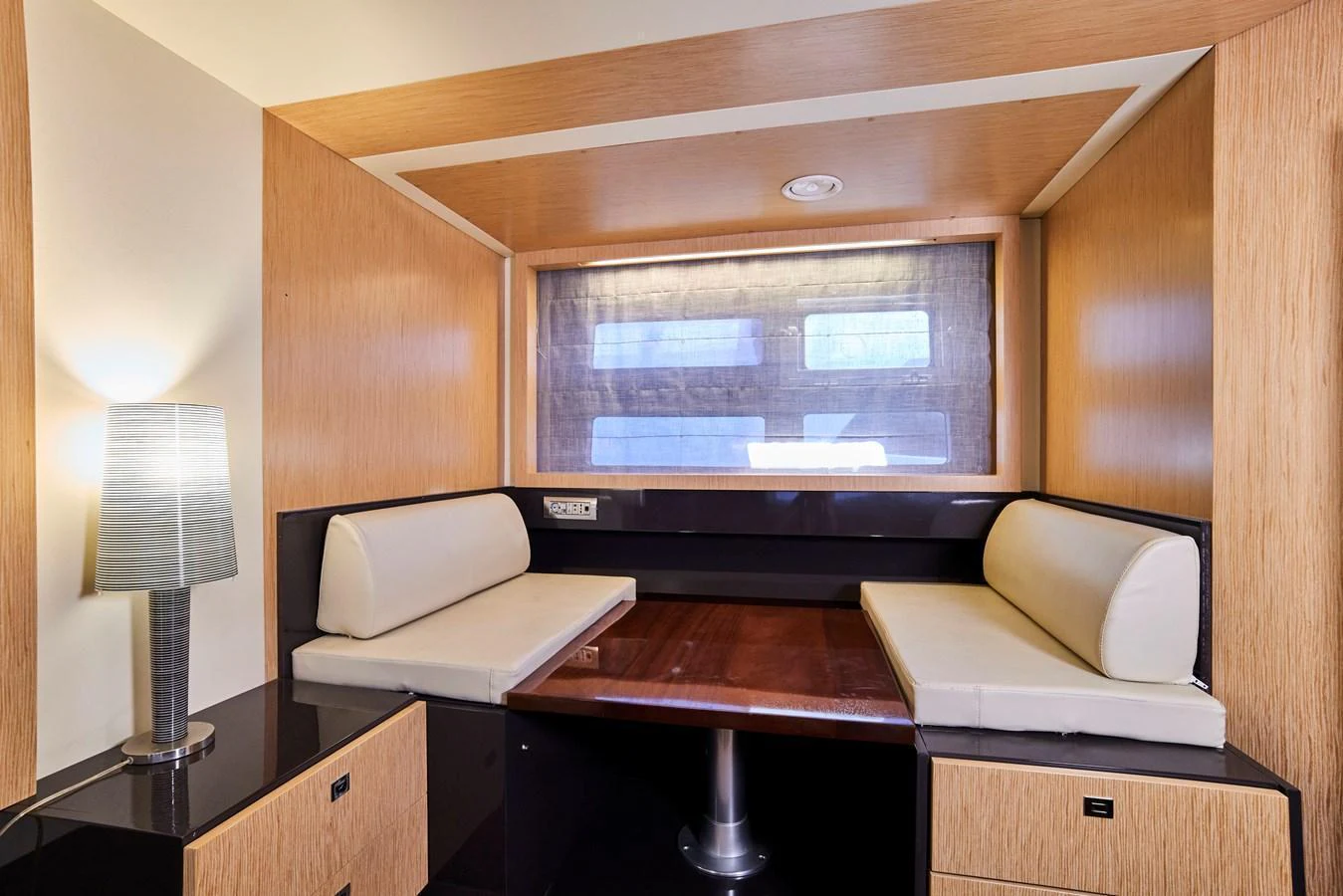 A cozy interior seating area with a wooden table and cushioned benches, illuminated by a modern lamp. aboard BAIA 70 Yacht for Sale
