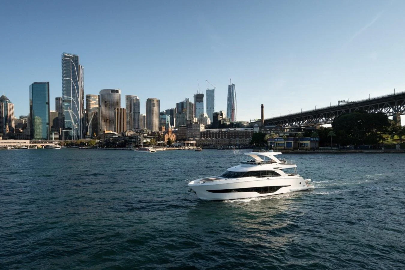 A sleek yacht cruises through the water with a city skyline and bridge in the background. aboard TOPAZ Yacht for Sale