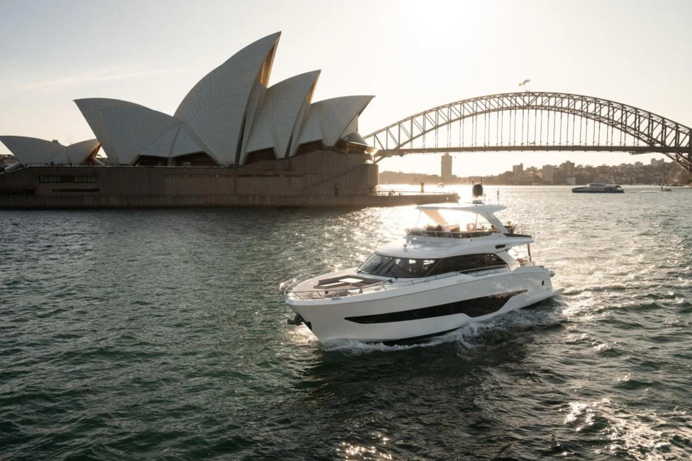 A sleek yacht cruises in front of iconic Sydney landmarks, showcasing its elegant design. aboard TOPAZ Yacht for Sale