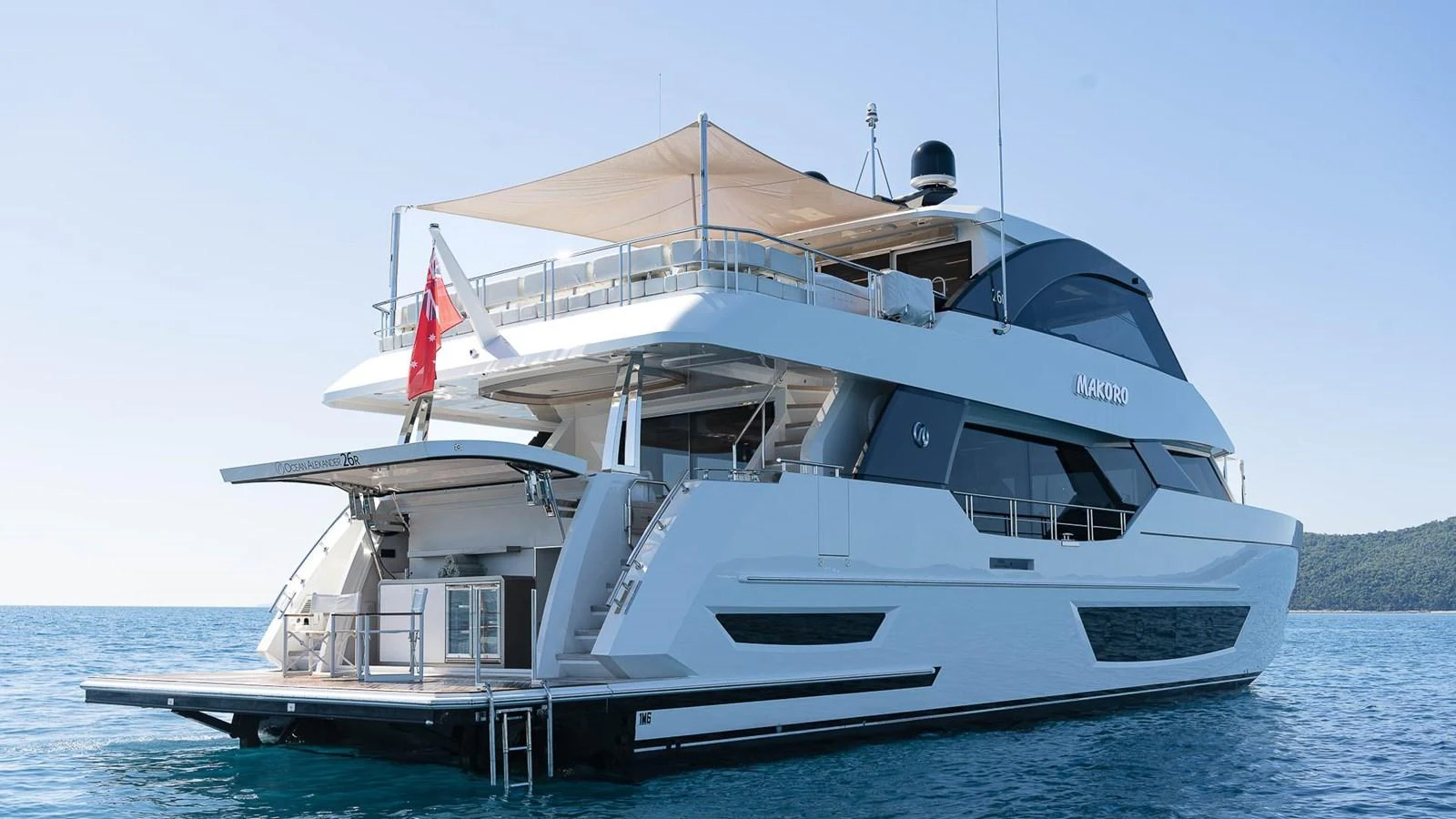 A sleek and modern yacht with multiple decks and a shaded area, cruising on calm blue waters. aboard MAKORO Yacht for Sale