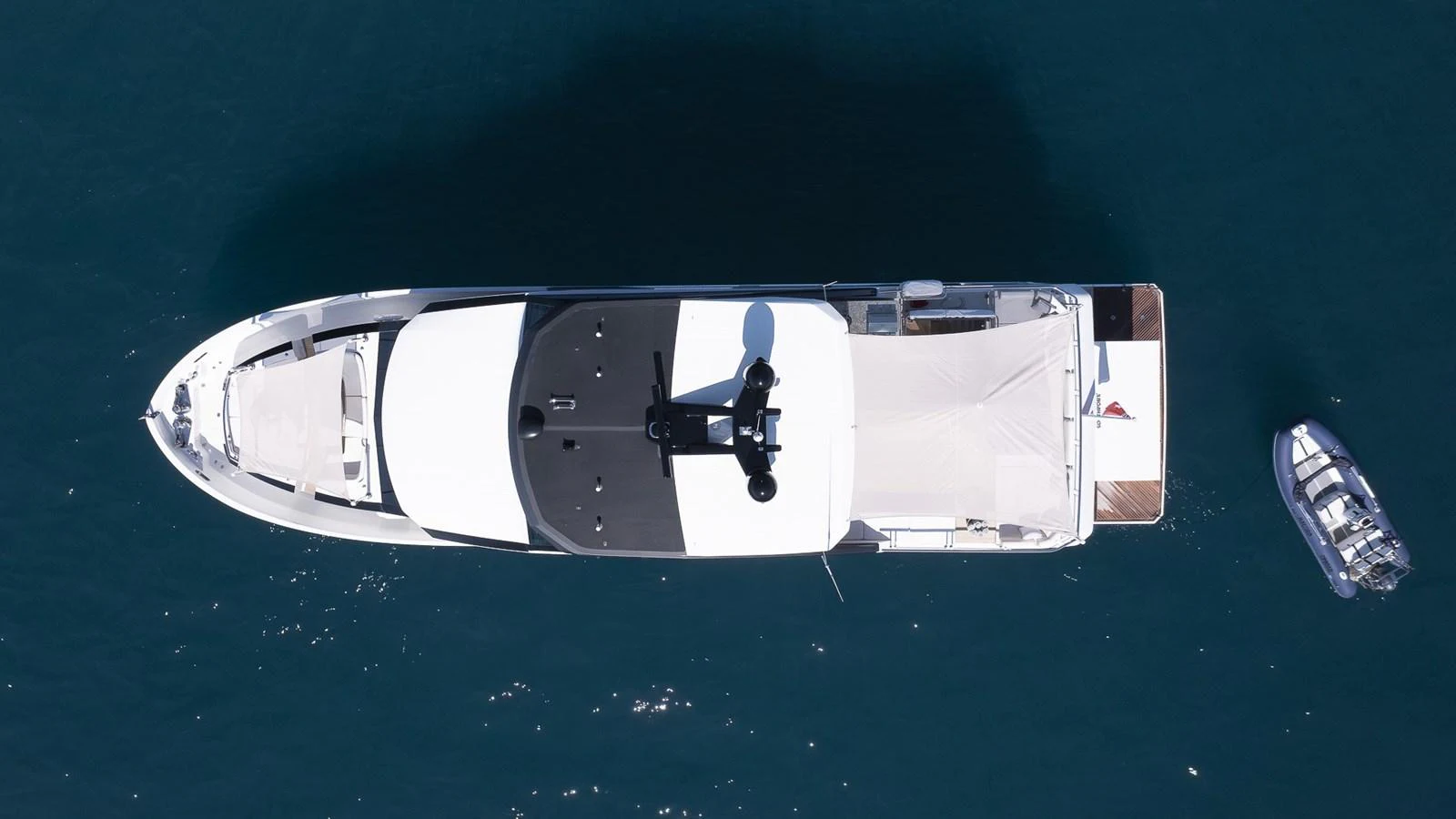 A stunning aerial view of a sleek yacht cruising on calm waters, accompanied by a tender. aboard MAKORO Yacht for Sale