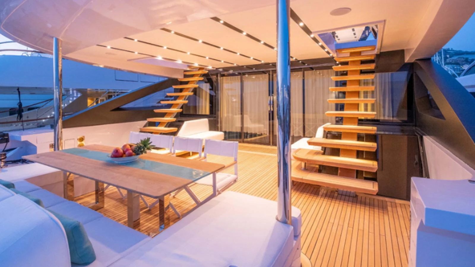 The aft deck features a spacious seating area with a dining table and elegant wooden stairs leading to the upper deck. aboard NEW Yacht for Sale