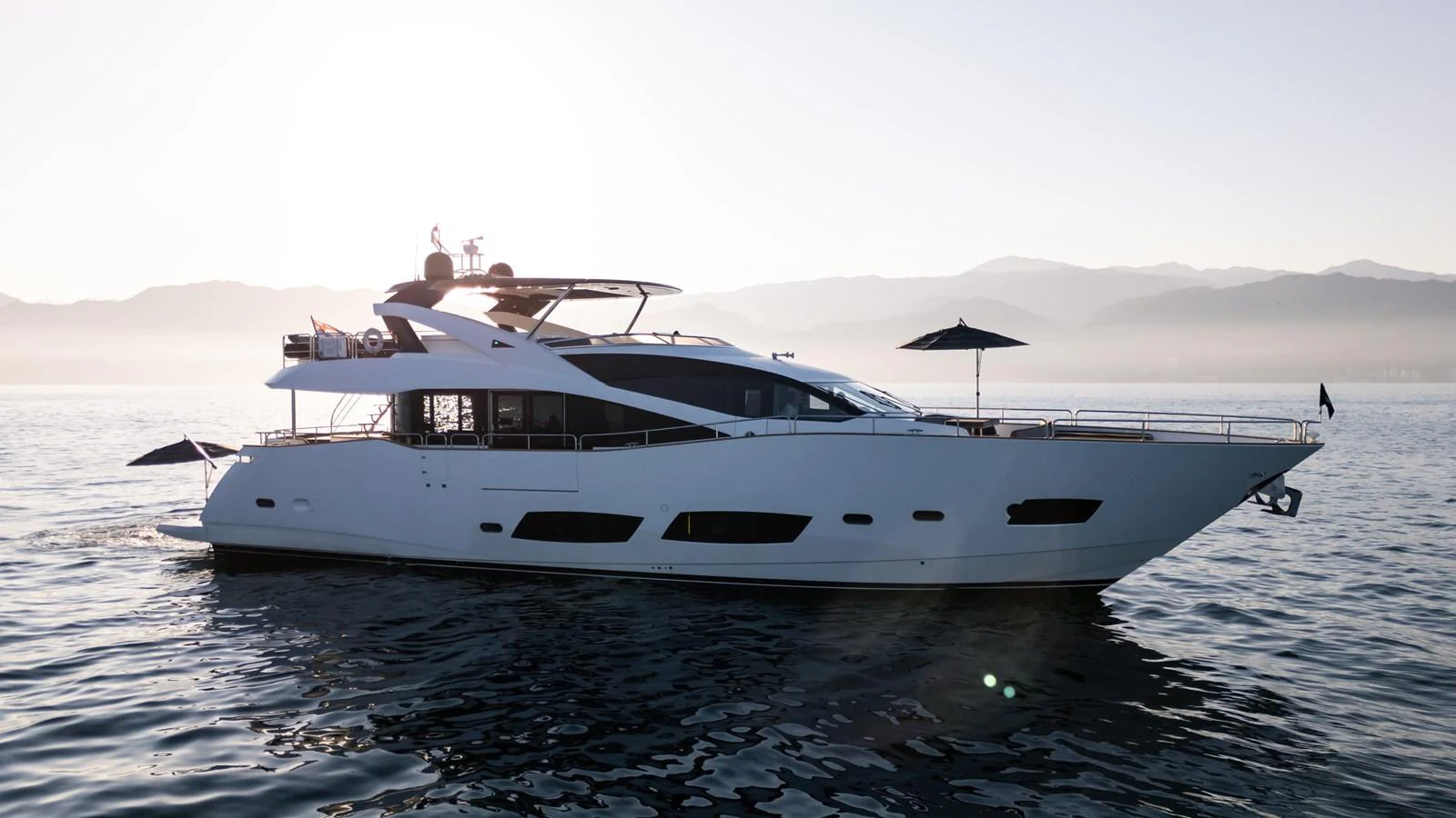 A sleek and modern yacht glides gracefully on calm waters with a stunning backdrop of misty mountains. aboard EBRA Yacht for Sale