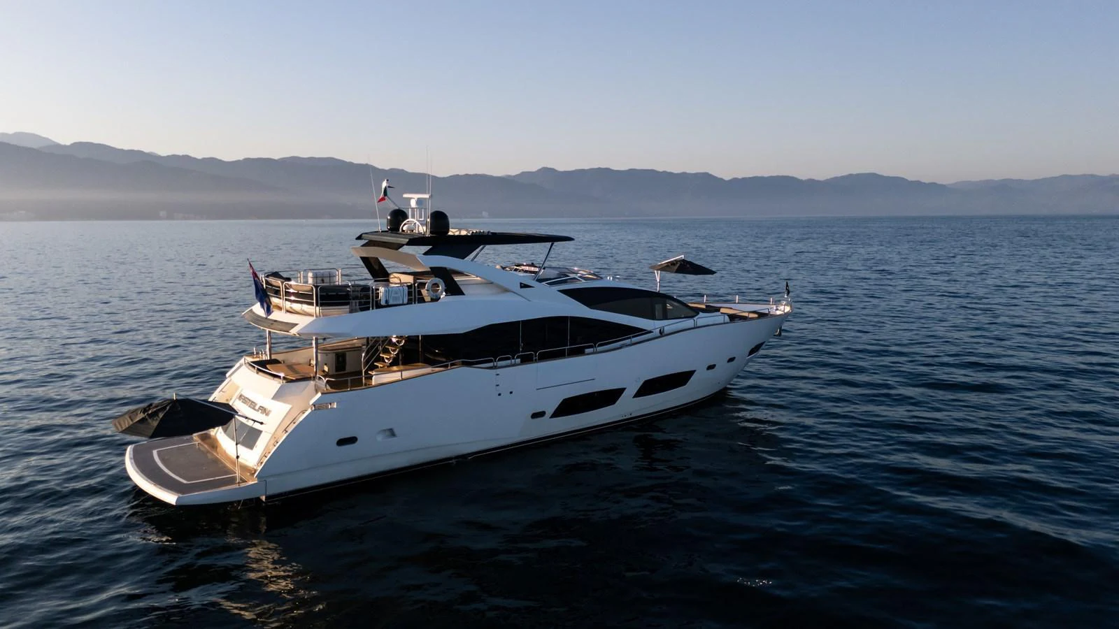 A sleek and modern yacht glides gracefully on calm waters with a mountainous backdrop. aboard EBRA Yacht for Sale