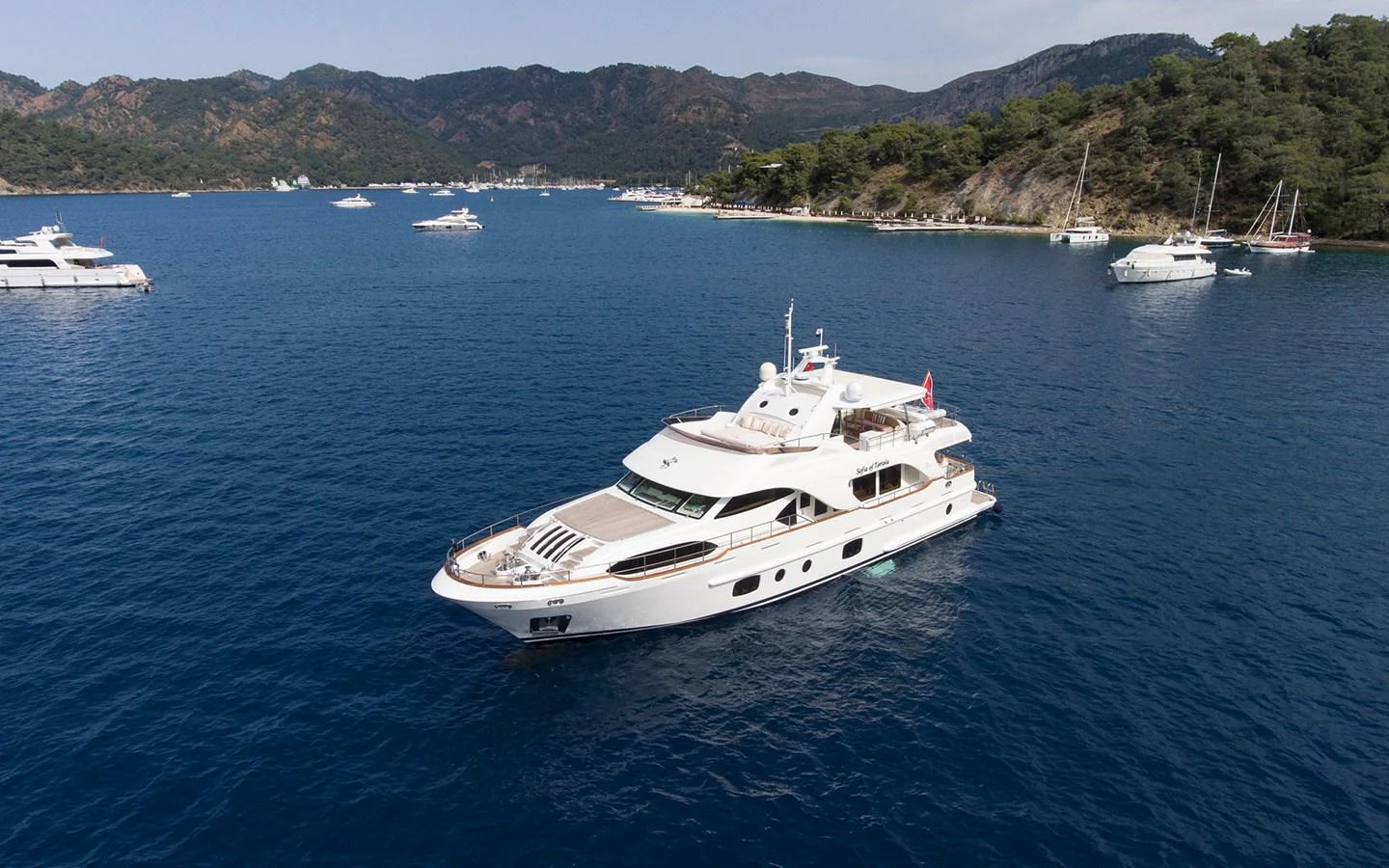 A luxurious yacht cruises through a serene bay with picturesque mountains in the background. aboard SOFIA OF TORTOLA Yacht for Sale