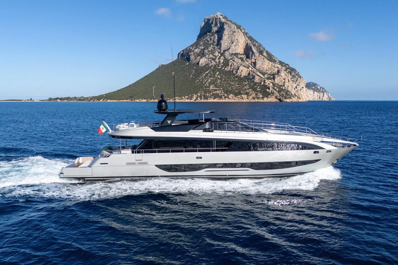 A sleek and modern yacht cruises through clear blue waters with a scenic mountainous backdrop. aboard FILIPPETTI F100-03 Yacht for Sale