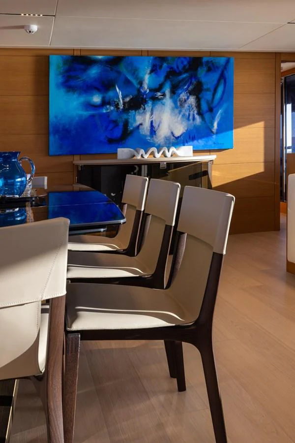 The yacht's dining area features modern chairs and a striking blue abstract painting on the wall. aboard FILIPPETTI F100-03 Yacht for Sale