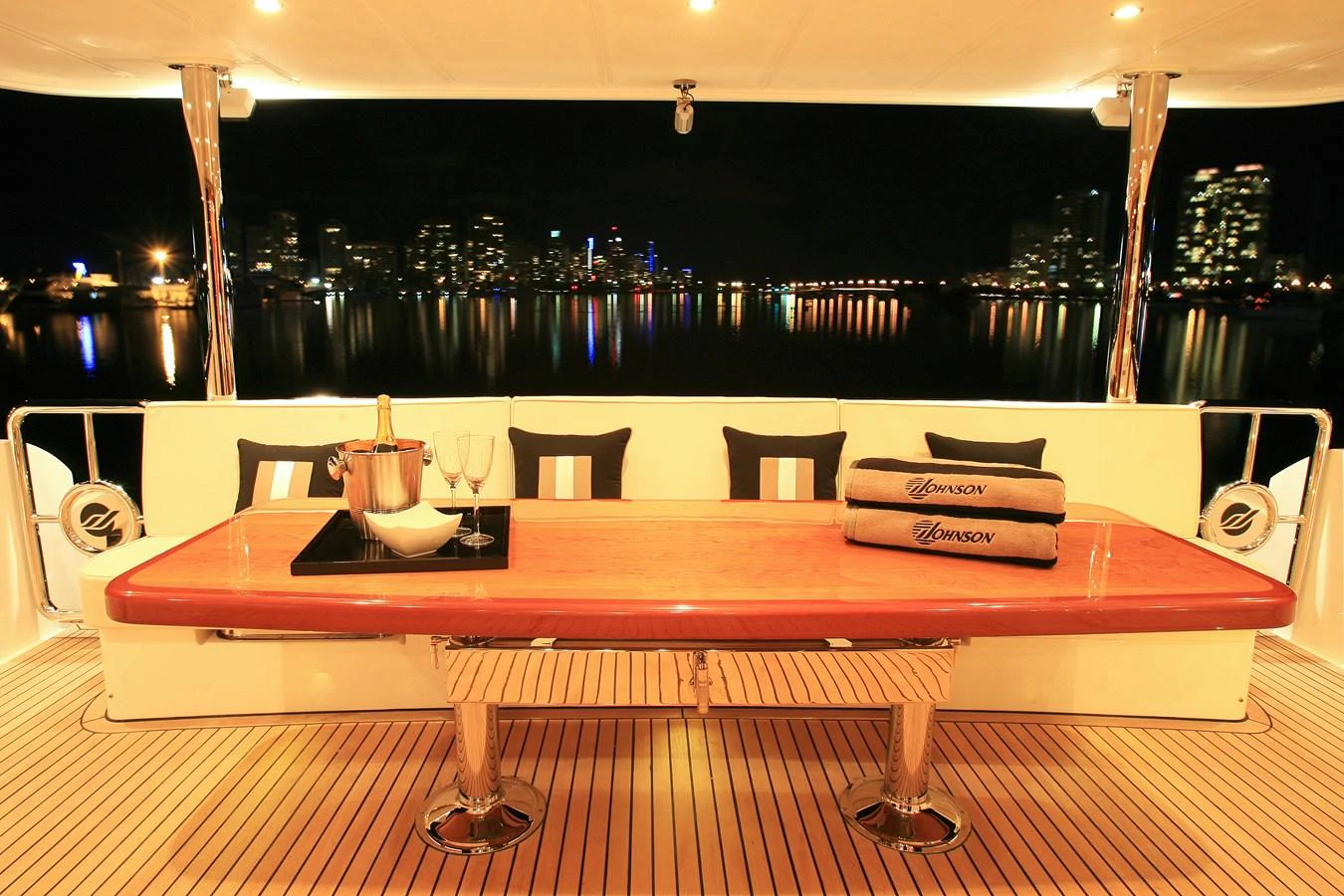 The aft deck features a stylish dining area with a city skyline view. aboard JOHNSON 83’ SKYLOUNGE W/FISHING COCKPIT Yacht for Sale
