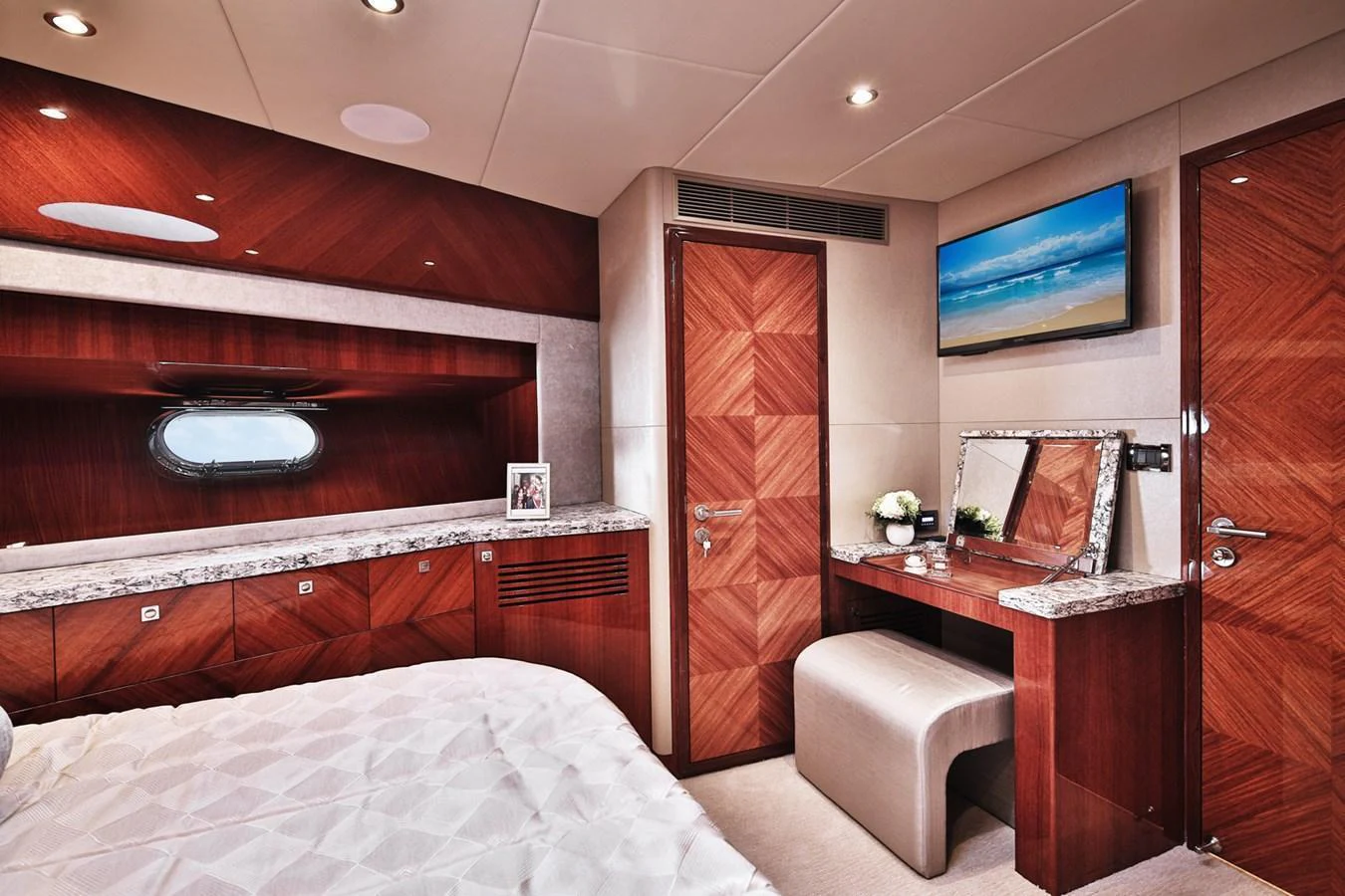 The stateroom features elegant wood finishes, a comfortable bed, and a vanity area with a scenic view on the TV. aboard JOHNSON 83' FLYBRIDGE W/HYDRAULIC PLATFORM Yacht for Sale