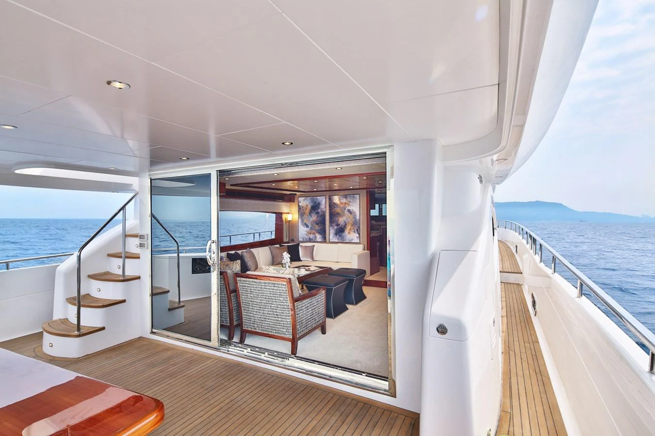 The aft deck seamlessly transitions into a luxurious interior living space with elegant furnishings. aboard JOHNSON 83' FLYBRIDGE W/HYDRAULIC PLATFORM Yacht for Sale