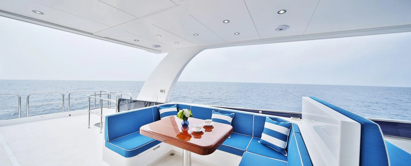 The aft deck features a stylish seating area with blue cushions and a wooden table, offering a perfect spot to enjoy the ocean view. aboard JOHNSON 83' FLYBRIDGE W/HYDRAULIC PLATFORM Yacht for Sale