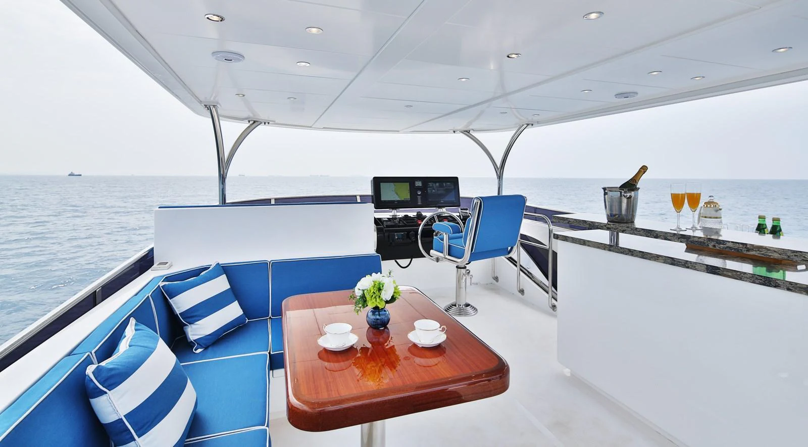 The flybridge offers a luxurious seating area with a table, a helm station, and a bar, all with a stunning ocean view. aboard JOHNSON 83' FLYBRIDGE W/HYDRAULIC PLATFORM Yacht for Sale
