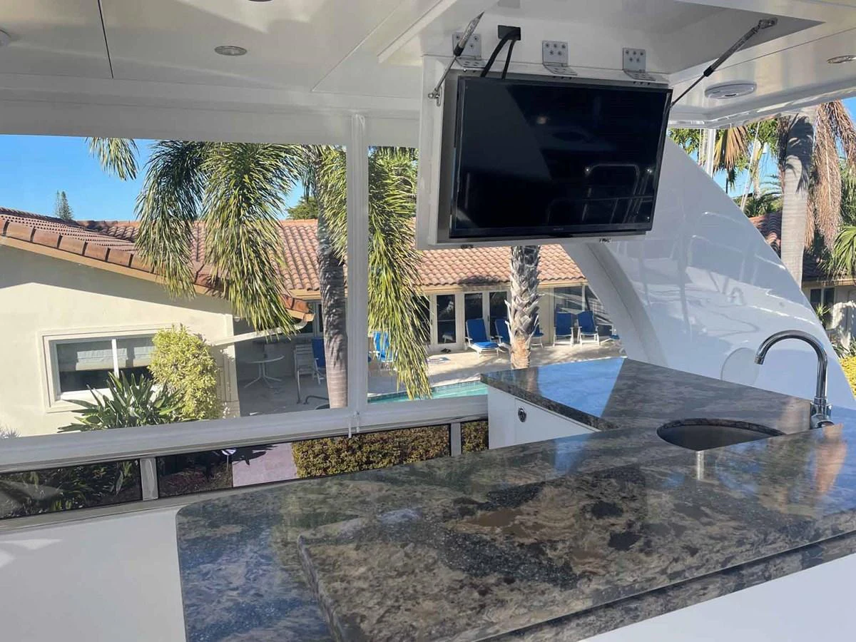 The yacht's galley features a sleek countertop with a built-in sink and a mounted TV for entertainment. aboard JOHNSON 83' FLYBRIDGE W/HYDRAULIC PLATFORM Yacht for Sale
