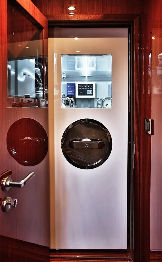 A sleek, modern door with a porthole window opens to reveal a high-tech control panel inside the yacht. aboard JOHNSON 83' FLYBRIDGE W/HYDRAULIC PLATFORM Yacht for Sale