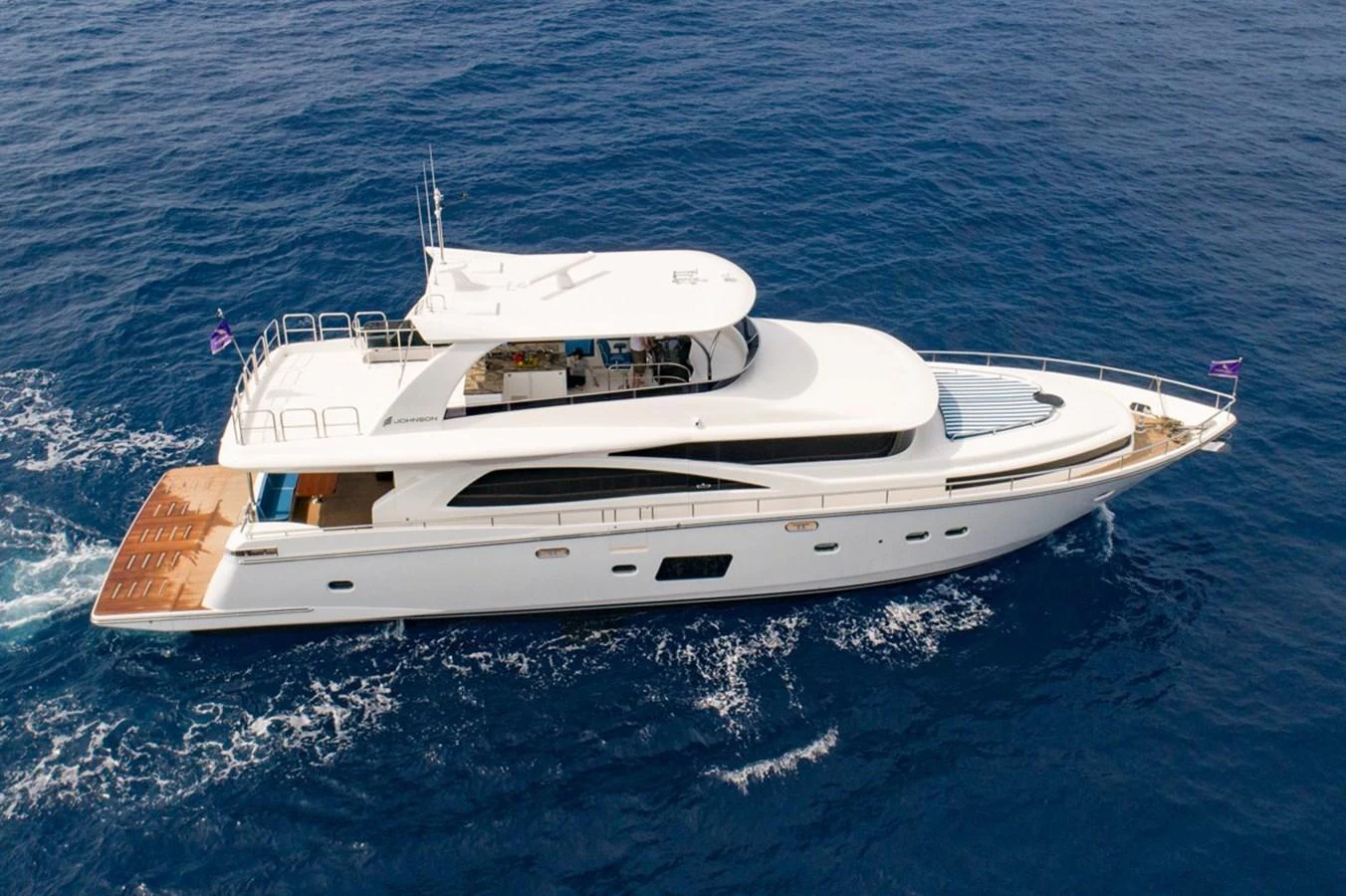 A sleek and modern yacht glides gracefully over the deep blue sea. aboard JOHNSON 83' FLYBRIDGE W/HYDRAULIC PLATFORM Yacht for Sale