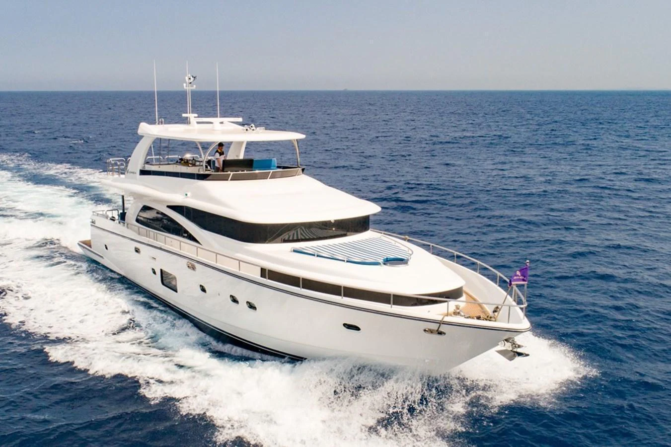 A sleek and modern yacht cruising on the open sea under clear skies. aboard JOHNSON 83' FLYBRIDGE W/HYDRAULIC PLATFORM Yacht for Sale