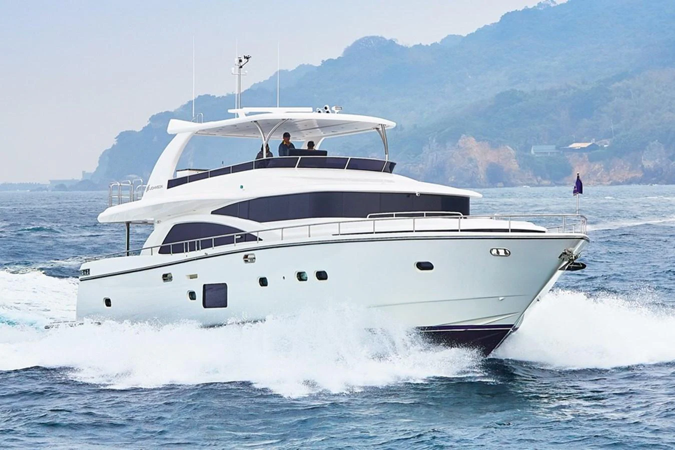 A sleek and modern yacht cruising through the water with a scenic backdrop. aboard JOHNSON 83' FLYBRIDGE W/HYDRAULIC PLATFORM Yacht for Sale
