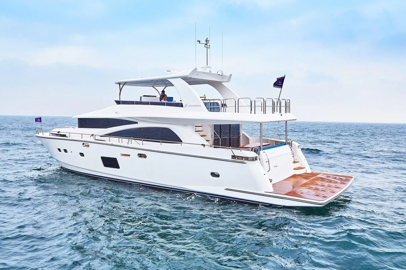 A sleek and modern yacht cruising on calm waters under a clear sky. aboard JOHNSON 83' FLYBRIDGE W/HYDRAULIC PLATFORM Yacht for Sale