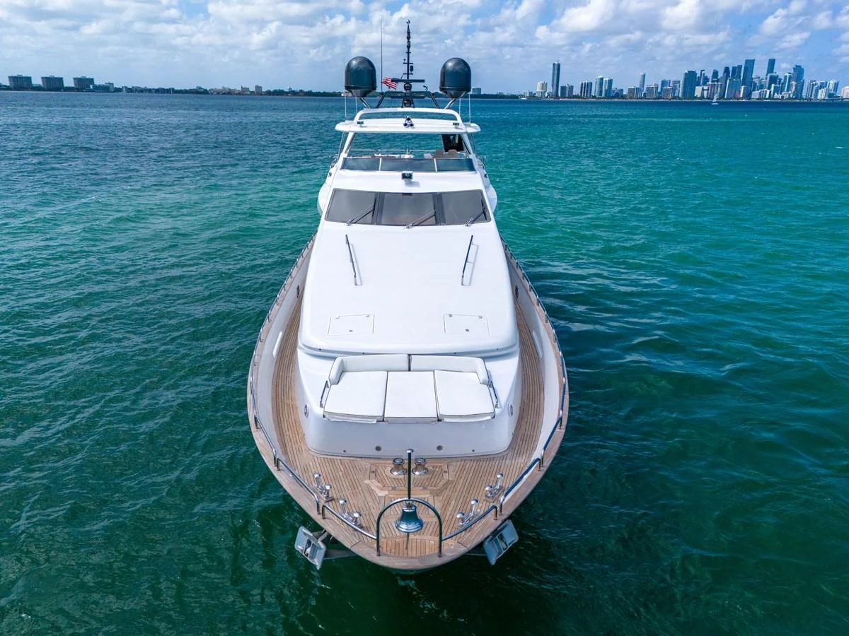 A sleek yacht cruises through clear blue waters with a cityscape in the background. aboard AZIMUT GRANDE 105 Yacht for Sale