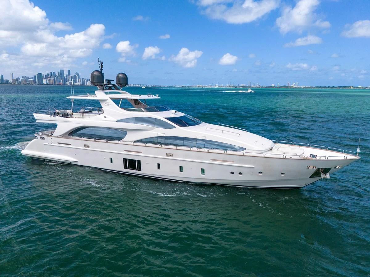 A sleek and modern yacht cruising on clear blue waters with a city skyline in the background. aboard AZIMUT GRANDE 105 Yacht for Sale