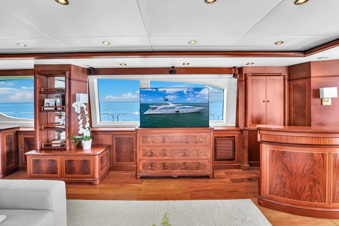 The yacht's interior features elegant wooden cabinetry and a large flat-screen TV with ocean views through the windows. aboard AZIMUT GRANDE 105 Yacht for Sale
