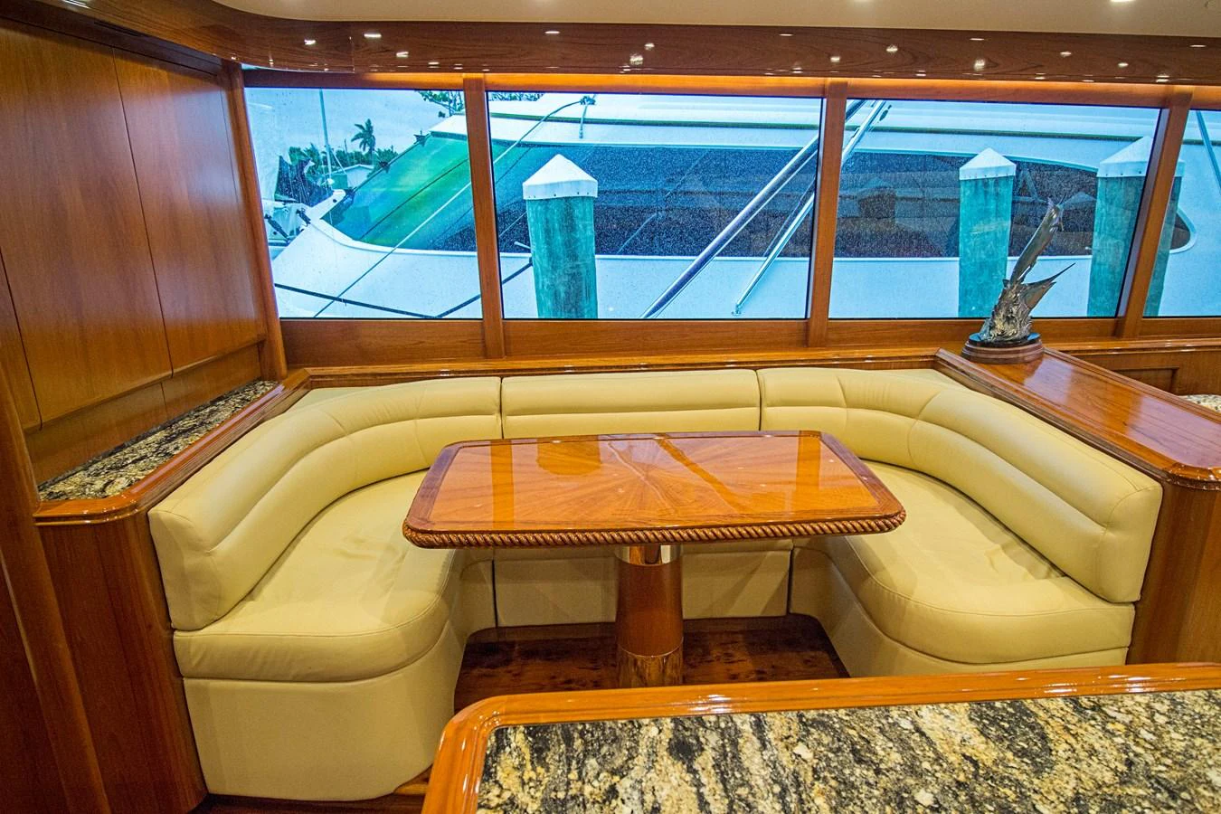 The yacht's dining area features a luxurious wooden table surrounded by plush seating and large windows offering a view of the marina. aboard REMAIN CALM Yacht for Sale