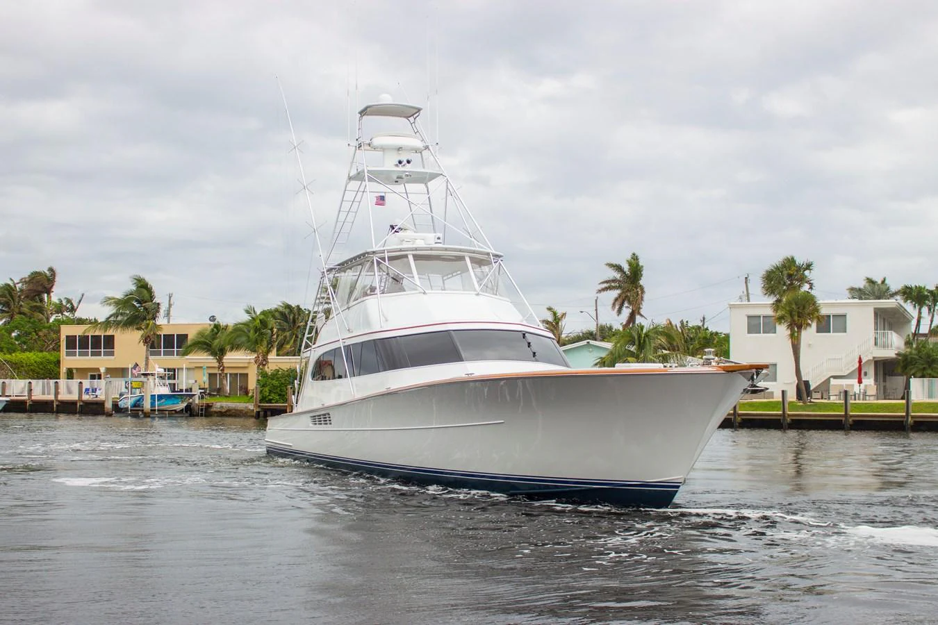 A sleek yacht cruises through a calm waterway with modern homes in the background. aboard REMAIN CALM Yacht for Sale