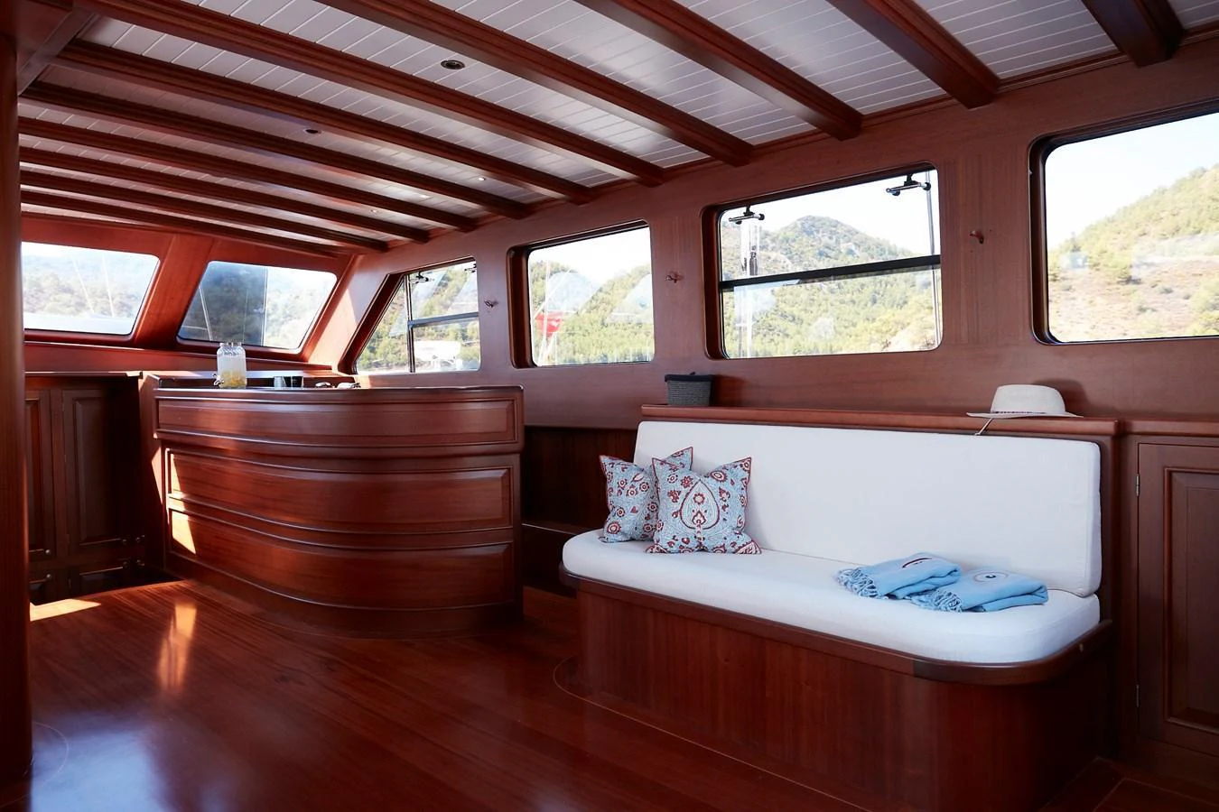 The salon features rich wood paneling, large windows, and a comfortable seating area with decorative pillows. aboard WHITE WINGS Yacht for Sale