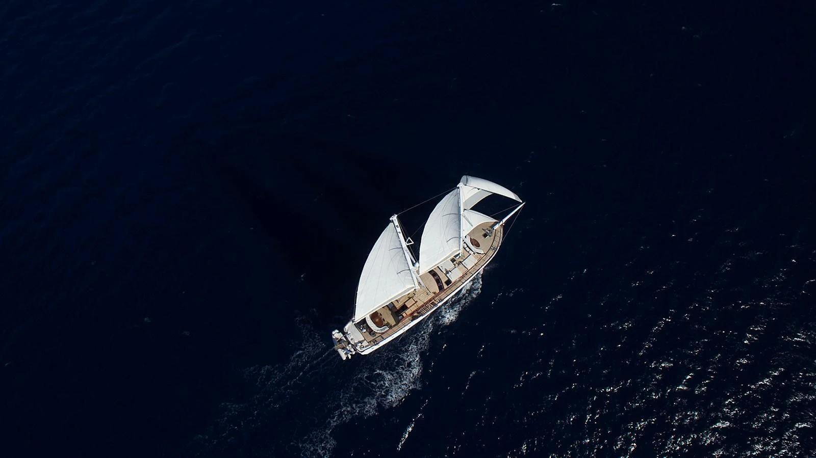 A stunning aerial view of a sailing yacht gracefully cutting through the deep blue sea. aboard WHITE WINGS Yacht for Sale