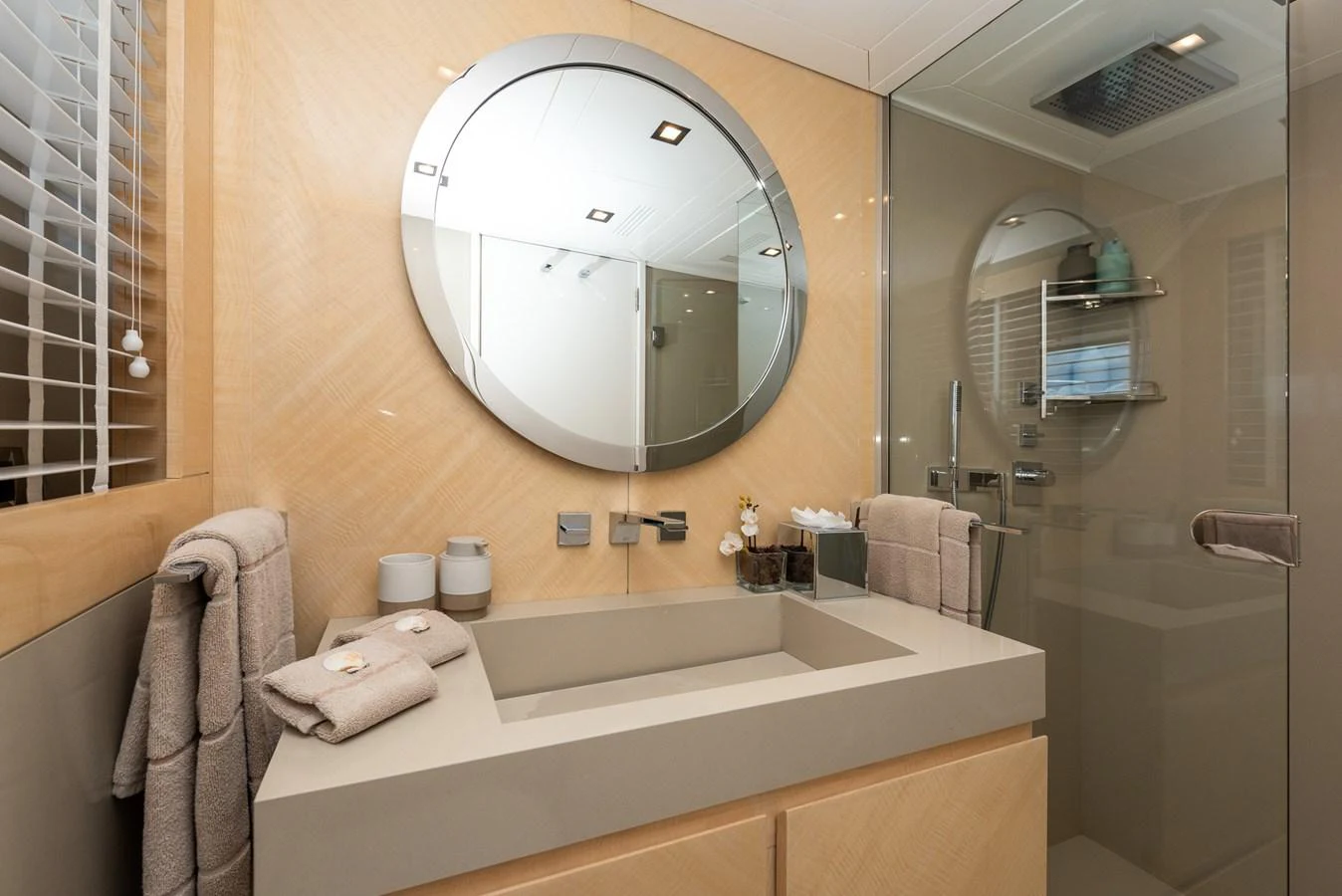 The yacht's bathroom features a modern sink, a large circular mirror, and a glass-enclosed shower. aboard NYLA Yacht for Sale