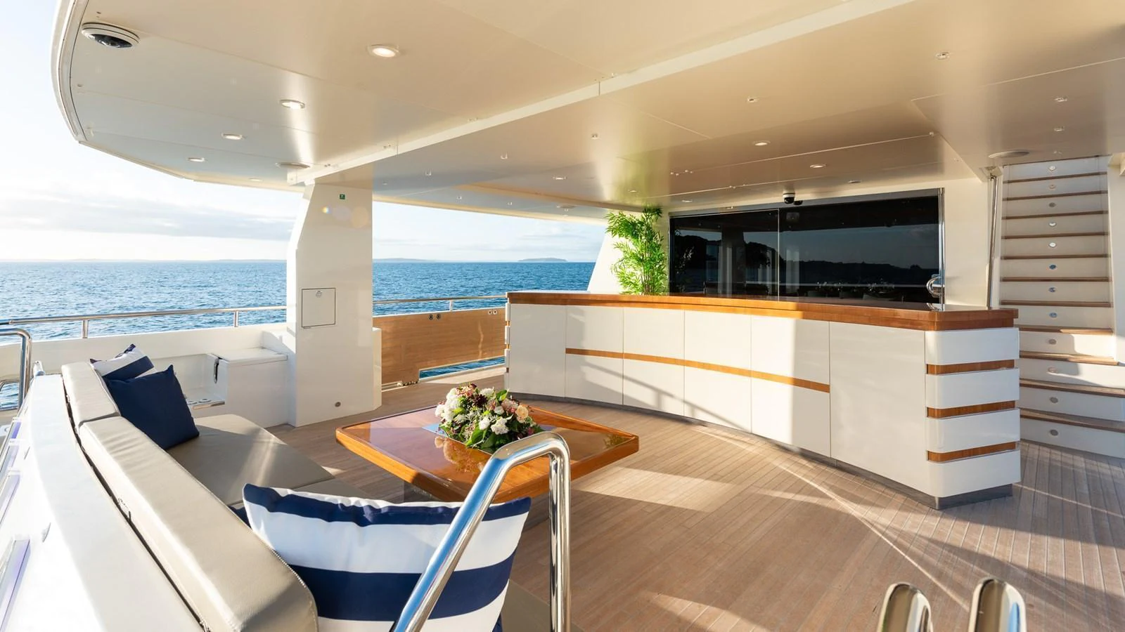 The aft deck features a spacious seating area with a wooden table and a sleek bar, perfect for enjoying the ocean view. aboard NYLA Yacht for Sale