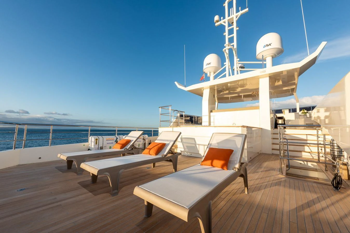 The sundeck features luxurious sun loungers with vibrant orange cushions, perfect for relaxation under clear skies. aboard NYLA Yacht for Sale
