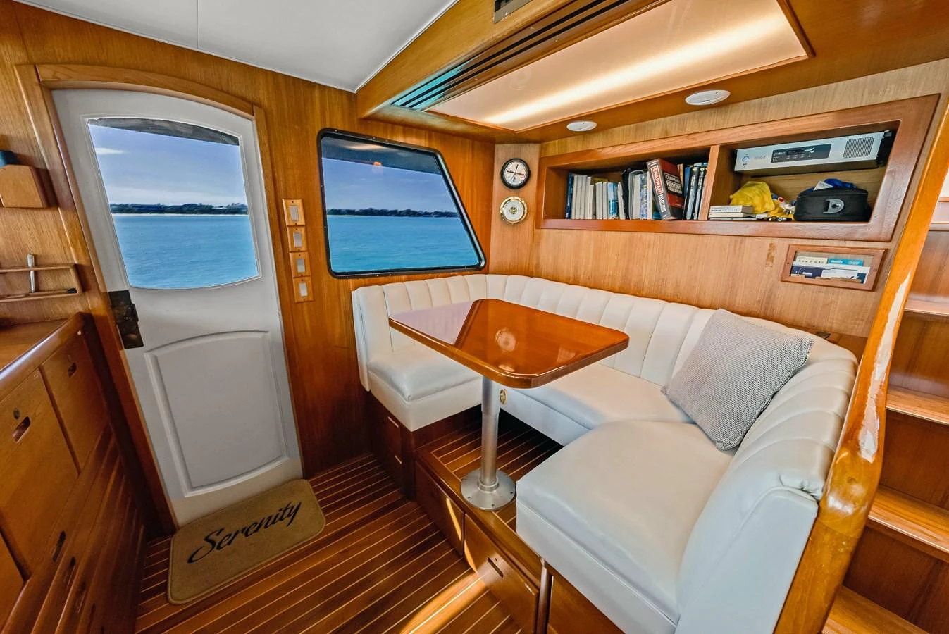 The cozy salon features a comfortable seating area with a wooden table, surrounded by windows offering serene ocean views. aboard SERENITY Yacht for Sale