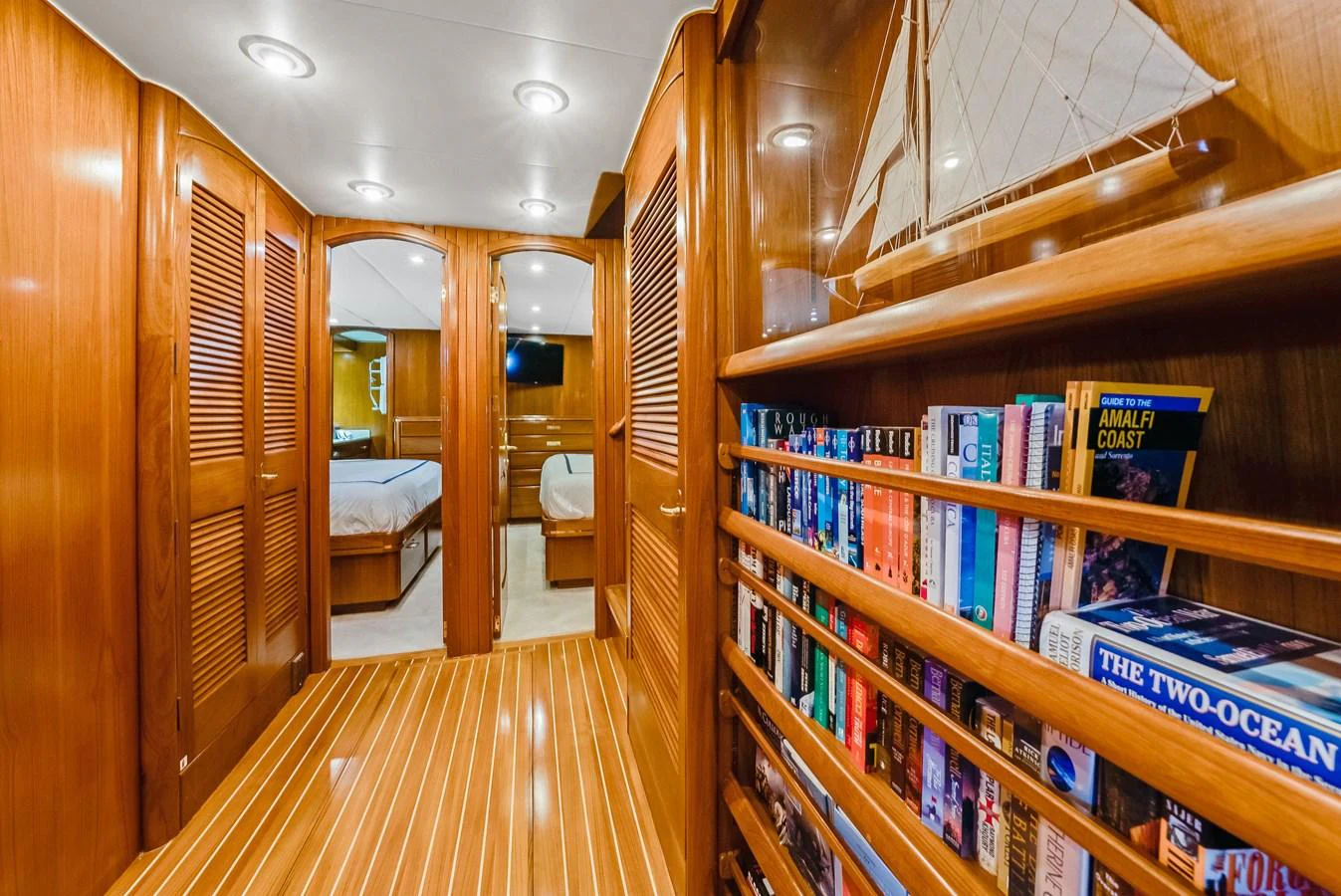 A warm and inviting yacht hallway with wooden finishes and a built-in bookshelf. aboard SERENITY Yacht for Sale