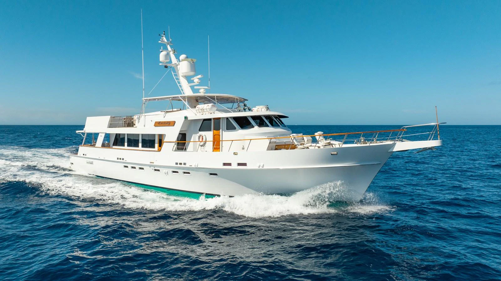 A sleek white yacht glides effortlessly through the open sea under a clear blue sky. aboard SERENITY Yacht for Sale