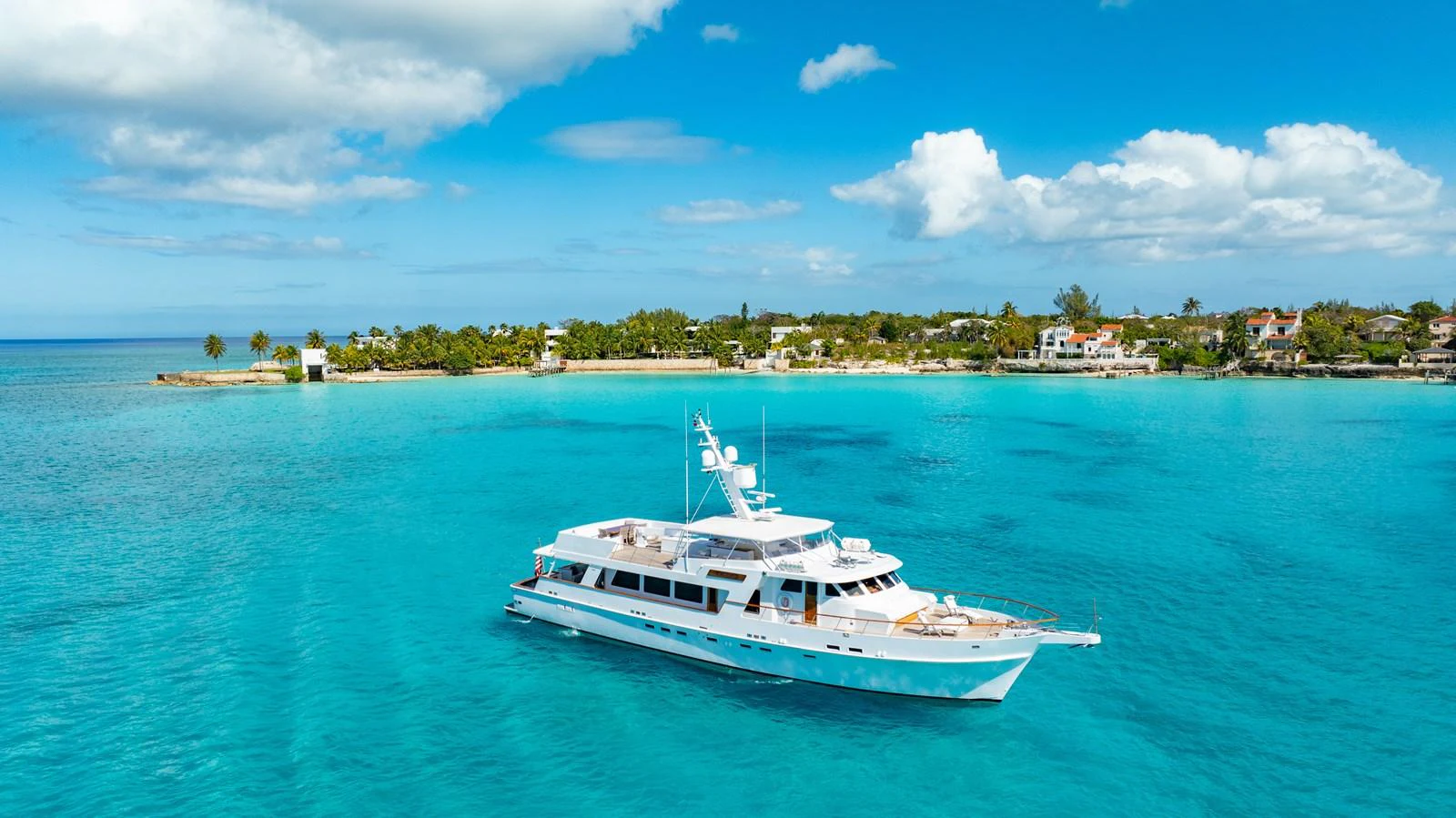 A luxurious yacht cruises through pristine turquoise waters near a picturesque shoreline. aboard SERENITY Yacht for Sale