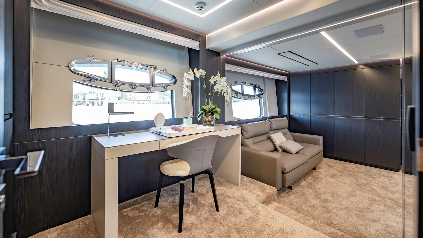 A luxurious office area with a desk, chair, and a comfortable seating arrangement, complemented by large windows for natural light. aboard ANDIAMO II Yacht for Sale