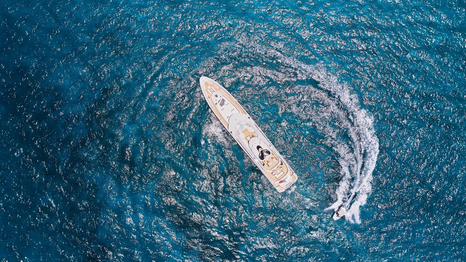An aerial view of a sleek yacht cruising through vibrant blue waters, leaving a dynamic wake behind. aboard ARKADIA Yacht for Sale