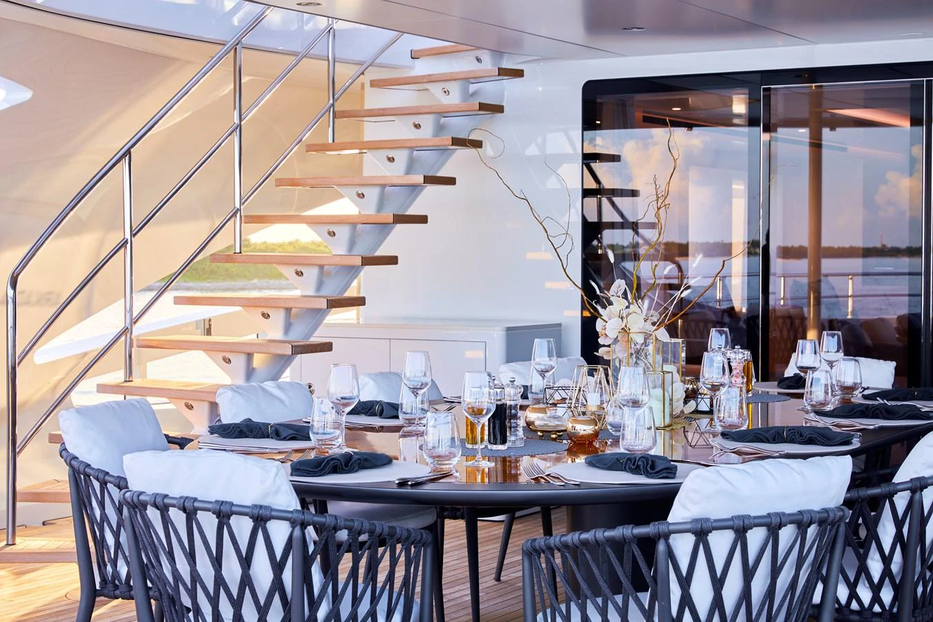 The aft deck features an elegant dining area with a beautifully set table and modern staircase. aboard ARKADIA Yacht for Sale