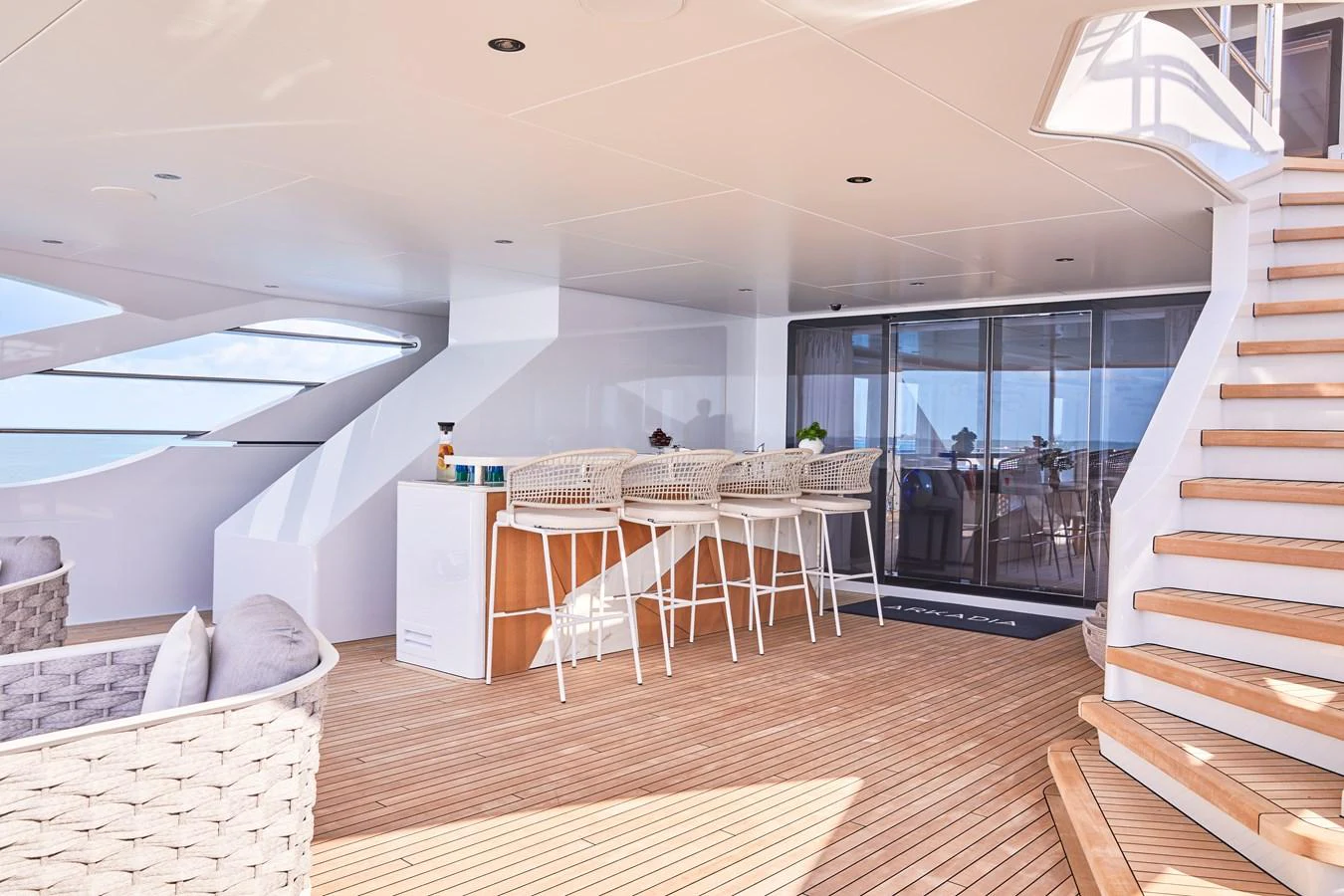 The aft deck features a stylish bar area with comfortable seating and a modern staircase leading to the upper deck. aboard ARKADIA Yacht for Sale