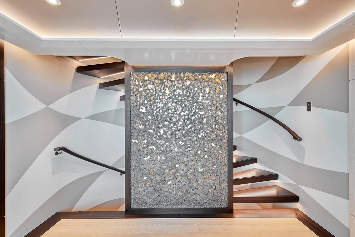 A modern yacht interior features a striking decorative wall panel and elegant staircases. aboard ARKADIA Yacht for Sale