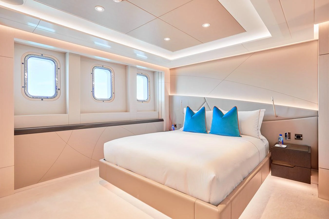 The stateroom features a luxurious bed with plush pillows and ample natural light from the porthole windows. aboard ARKADIA Yacht for Sale