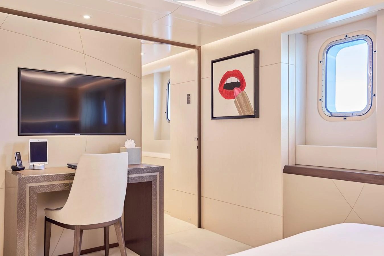 A stylish and modern yacht stateroom featuring a desk, a wall-mounted TV, and a porthole window. aboard ARKADIA Yacht for Sale