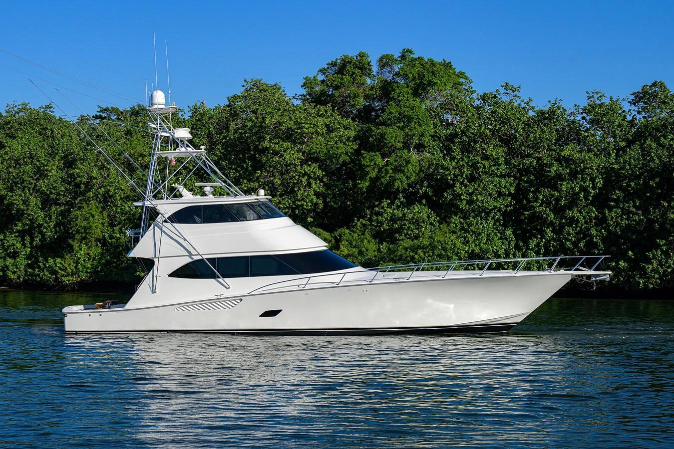 A sleek white yacht is cruising on calm waters with lush greenery in the background. aboard WASABI Yacht for Sale