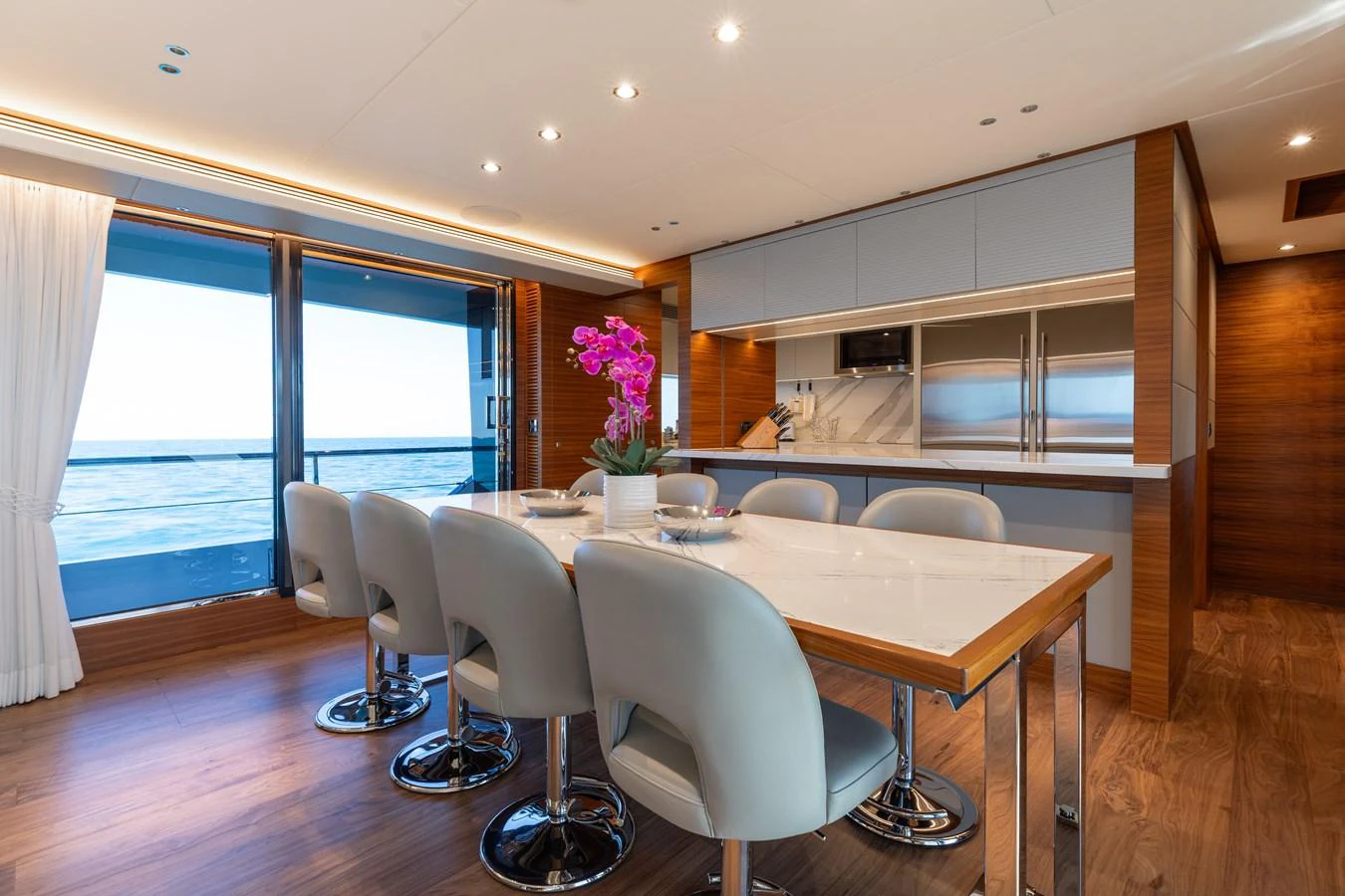 The yacht's dining area features a modern table with plush seating and a view of the ocean through large windows. aboard NEX-T Yacht for Sale