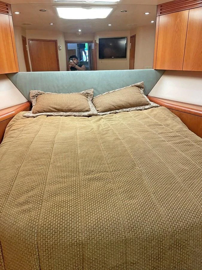 The cozy stateroom features a comfortable bed with warm wooden accents and soft lighting. aboard HATTERAS 68 CONVERTIBLE Yacht for Sale