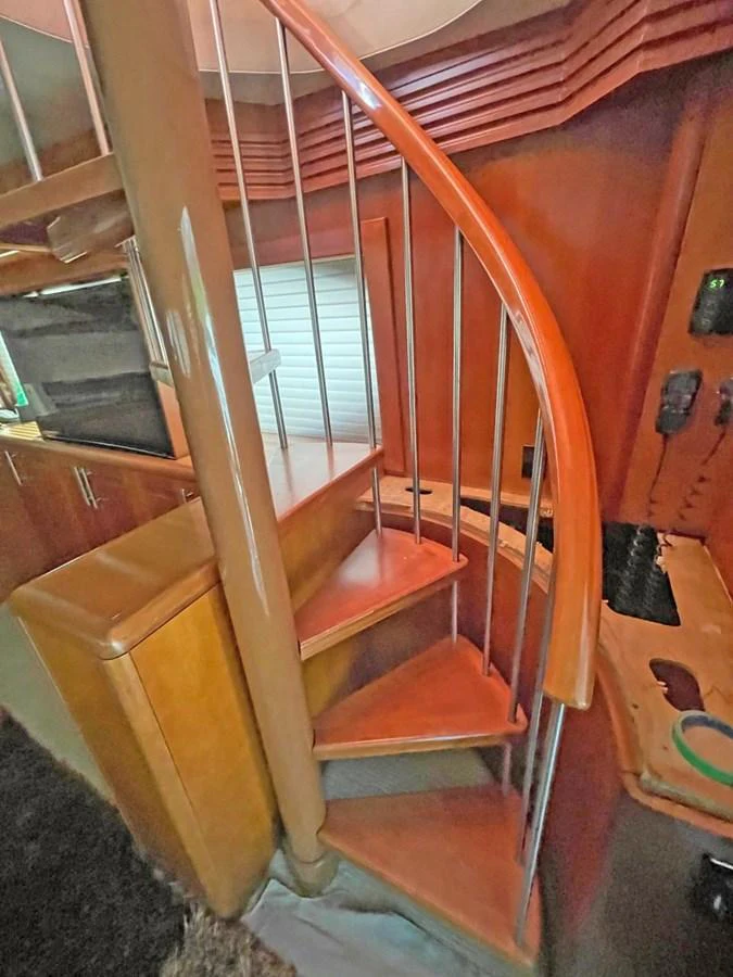 A stylish wooden spiral staircase leads to the upper deck, showcasing the yacht's elegant interior design. aboard HATTERAS 68 CONVERTIBLE Yacht for Sale